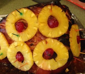 Adding pineapple slices and cherries to a ham before cooking.