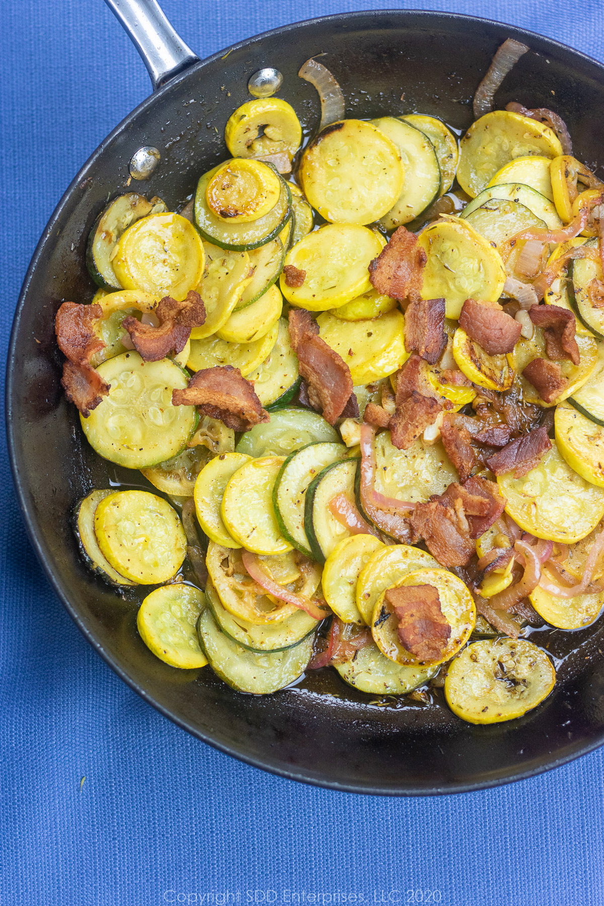 sautéed yellow squash and zucchini with bacon pieces in a skillet.