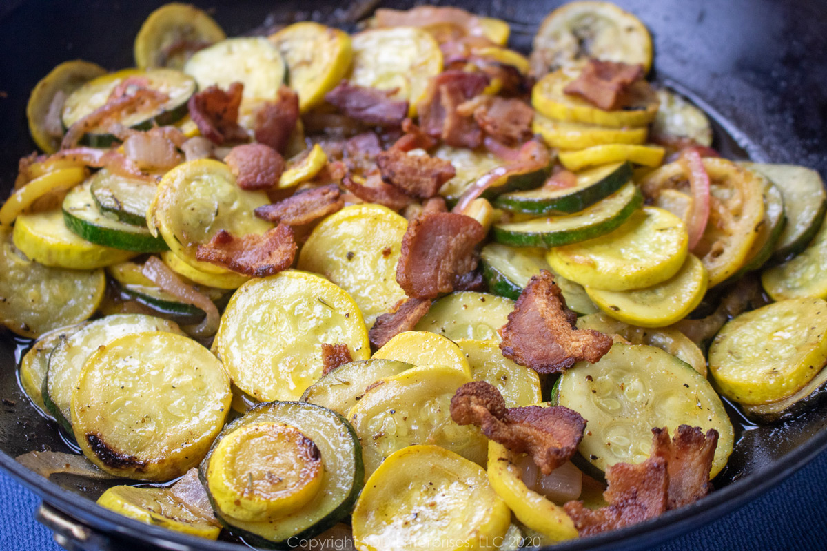 fresh yellow squash and zucchini isn a saute pan with onions, garlic and bacon