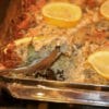 Stuffed Artichoke Casserole with lemon slices being spooned out of casserole