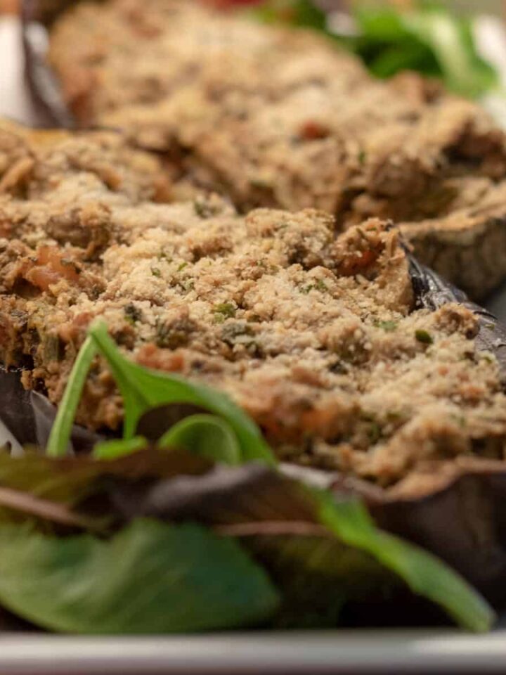 Roasted eggplant stuffed with shrimp and vegetables on a platter with garnishment