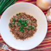 cajun dirty rice in a white bowl with green onions, yellow onion, garlic and fork