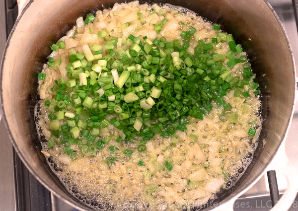 Adding green onions to onions and celery in a dutch oven