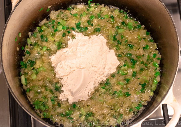 Adding flour to butter and onions and celery to make a blond roux