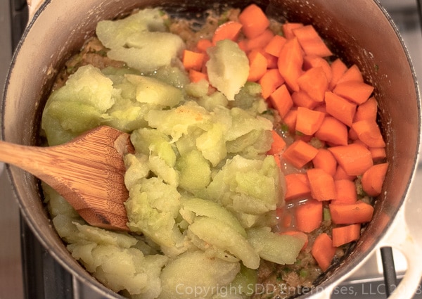 Mirlitons and carrots added to onions and celery in dutch oven