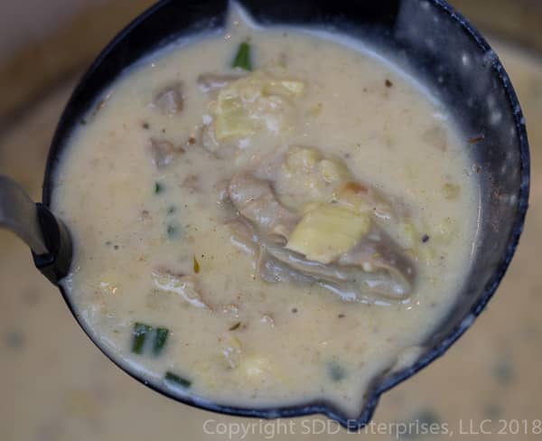 ladel full of oyster artichoke bisque with big oyster and artichoke