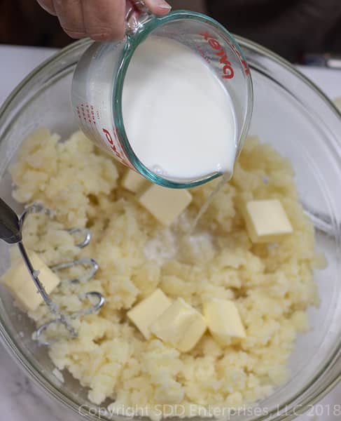 pouring milk into the potatoes and butter