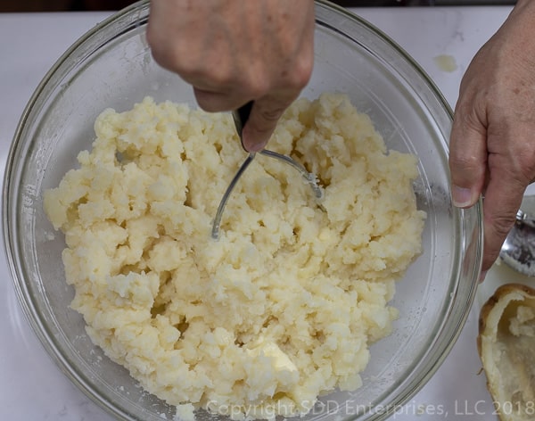 using a potato masher on the potatoes with milk and butter