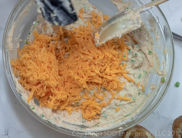 adding grated cheddar cheese to the potatoes