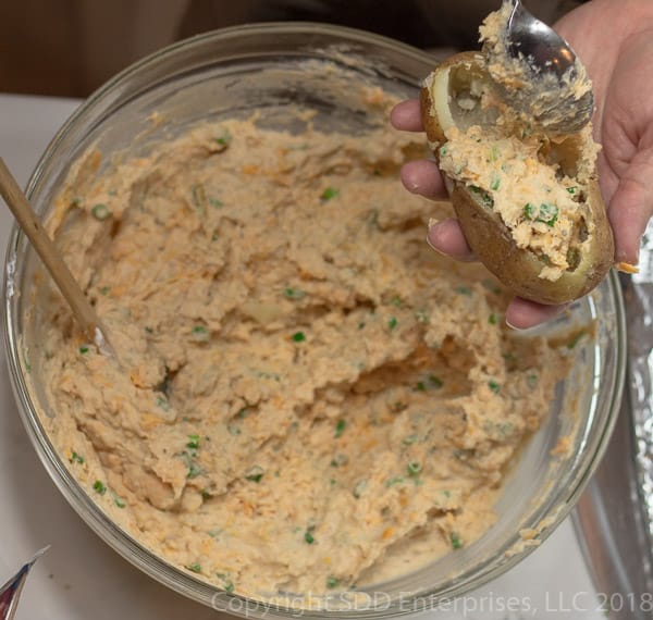 stuffing all the ingredients for twice baked potatoesadding grated cheddar cheese to the potatoes