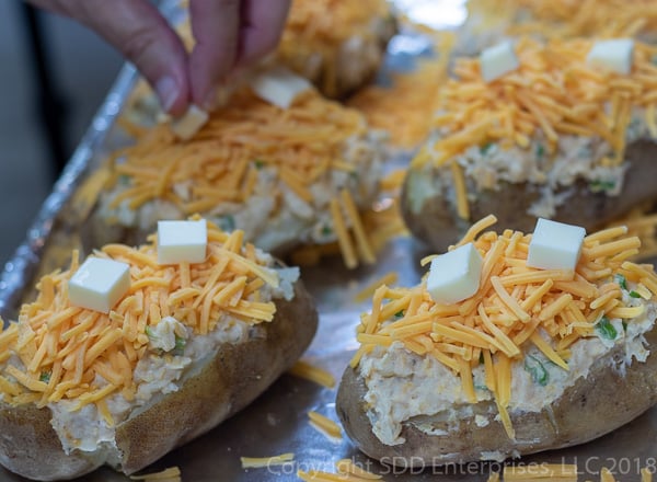 topping the stuffed potatoes with cheese and butter