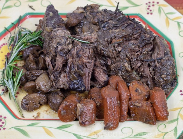 pot roast on a platter with carrots and mushrooms and rosemary