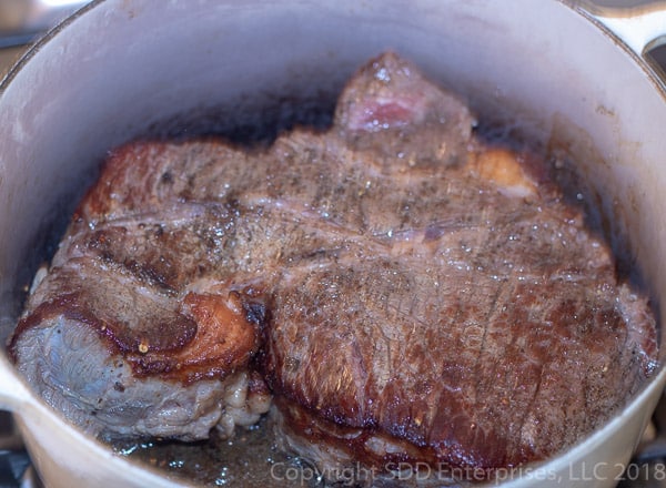 chuck roast being seared in a dutch oven