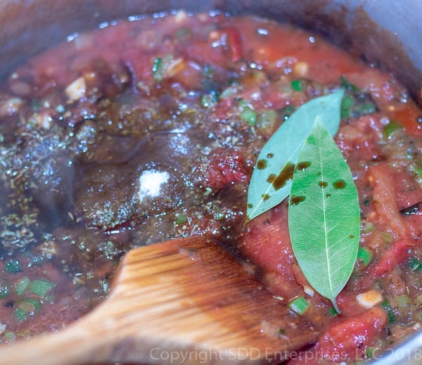 adding the sugar, juices and bay leaves to simmering creole sauce 