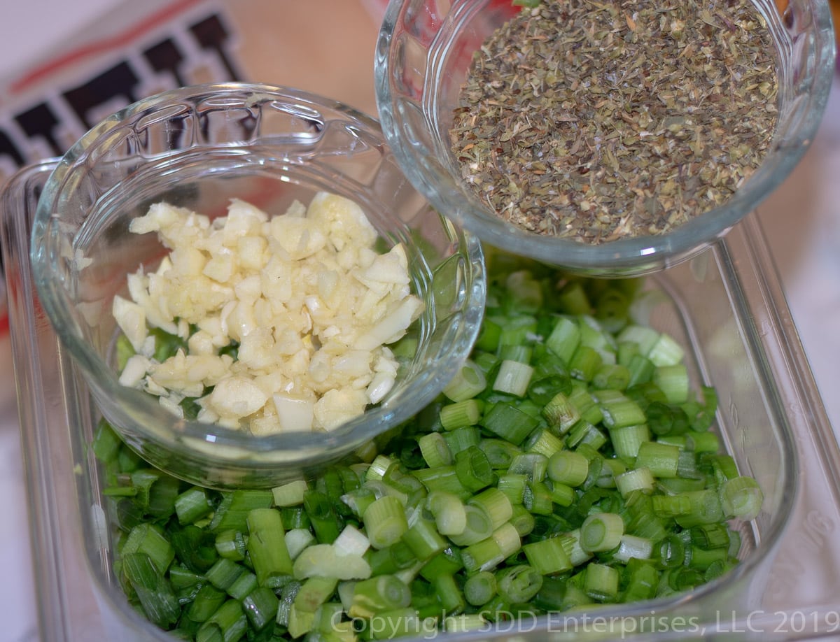 chopped garlic, herbs and spices in bowls with chopped yellow onions, celery , bell peppers and green onions.
