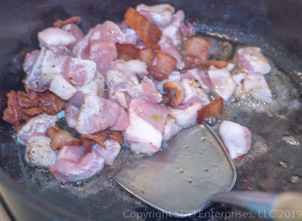 frying cubed pork and bacon in a dutch oven fro cajun jambalaya