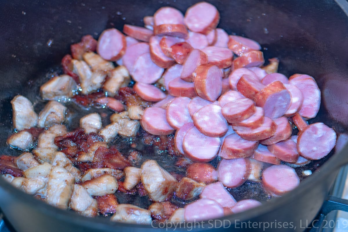 frying andouille sausage in a dutch oven with pork and bacon