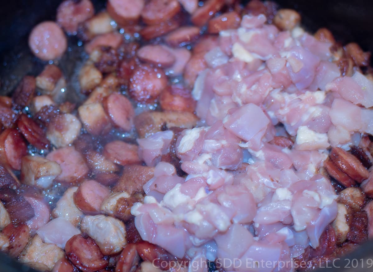 cubed chicken thighs added to dutch oven with sausage and pork