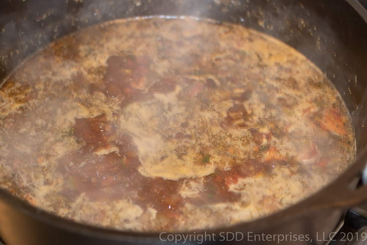 stock simmering in a dutch oven with meats and vegetables for cajun jambalaya