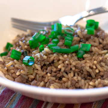 dirty rice in a white bowl with green onion garnish and a fork