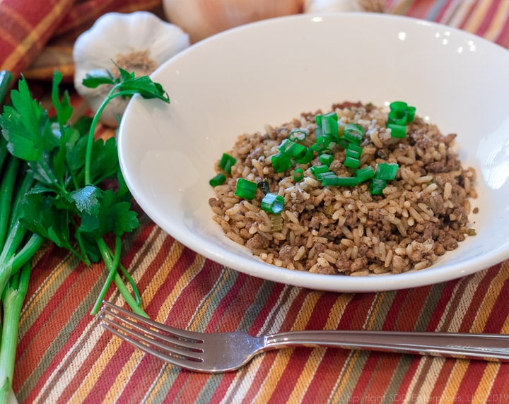 Cajun Dirty Rice in a white bowl with green onion garnish with fork