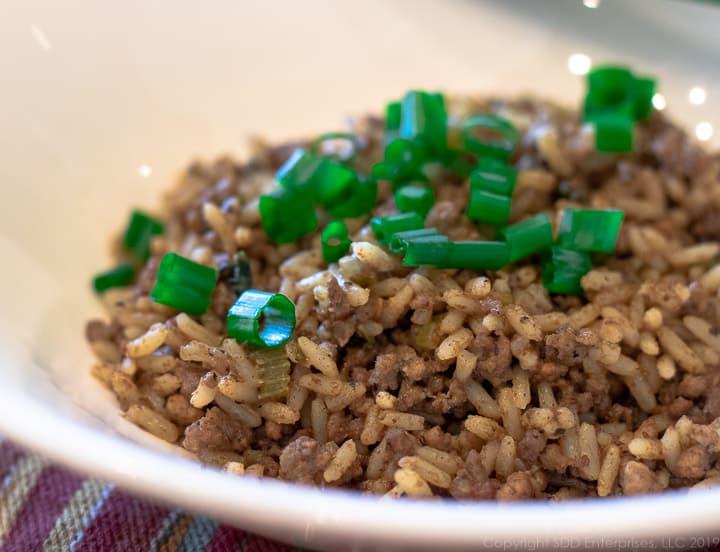 dirty rice in a white bowl garnished with chopped green onions