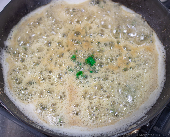 chopped green onions added to a developing roux in a cast iron pan for meuniere sauce