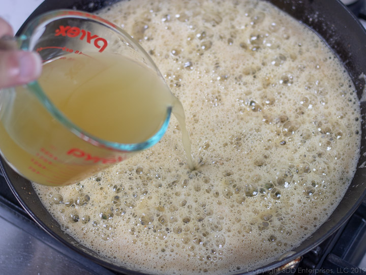 adding stock to the roux in a cast iron pan for meuniere sauce