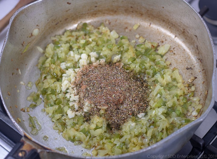 seasonongs and garlic added to onions and peppers in a frying pan