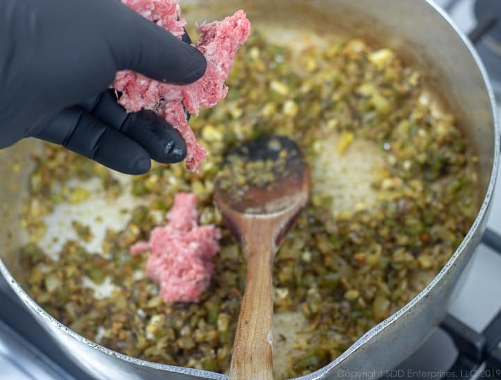 adding ground meat by hand to the frying pan with onions and peppers