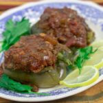 two stuffed bell peppers with creole sauce on a blue and white platter garnished with lemon slices and parsley