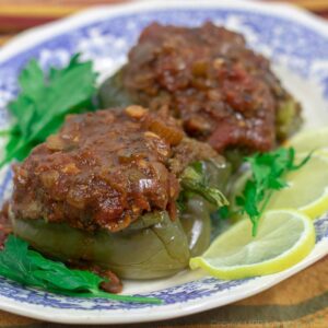 two stuffed bell peppers with creole sauce on a blue and white platter garnished with lemon slices and parsley