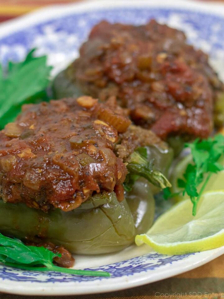 two stuffed bell peppers with creole sauce on a blue and white platter garnished with lemon slices and parsley
