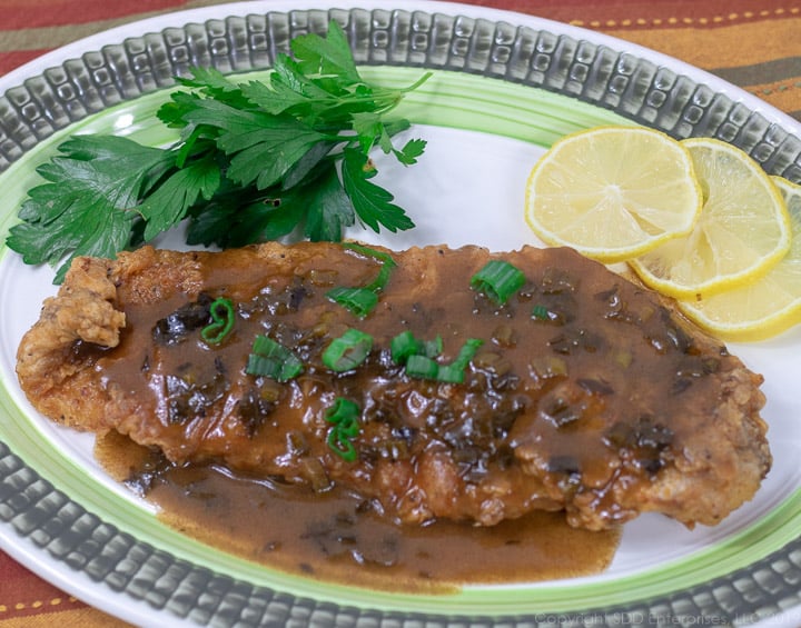 fried trout with meuniere sauce on a green rimmed platter and garnished with parsley and lemon slices