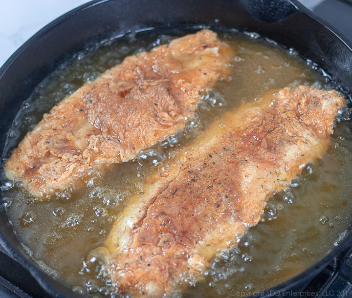 two fish filets frying in a cast iron pan