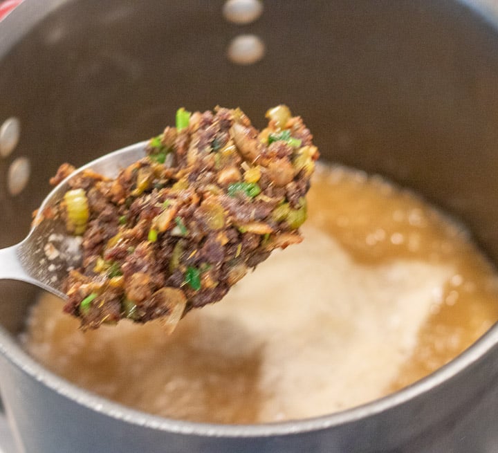 spoonful of roux/veggies being added to the stock in a stockpot for turkey oyster gumbo