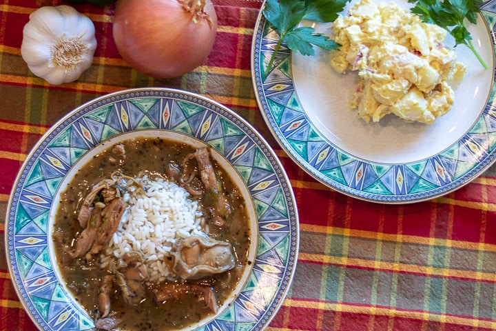 turkey oyster gumbo in a bowl with a plate of potato salad and garnishment