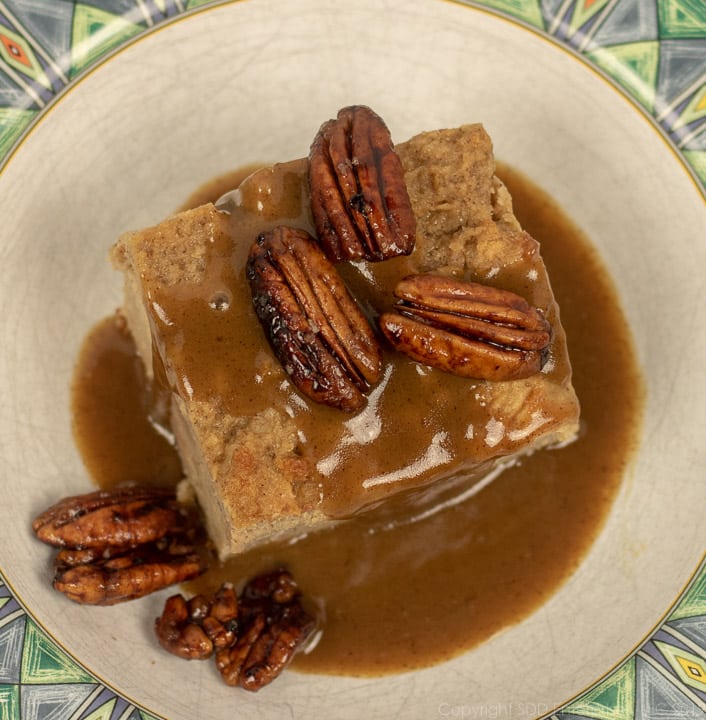 bread pudding with cane syrup sauce topped with pecans in a white bowl with green trim