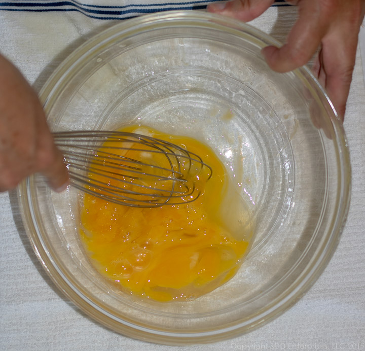 whisking eggs in a clear bowl for bread pudding