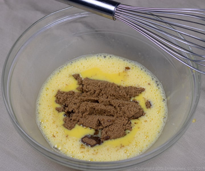 dark brown sugar added to whisked eggs in a clear glass bowl for bread pudding