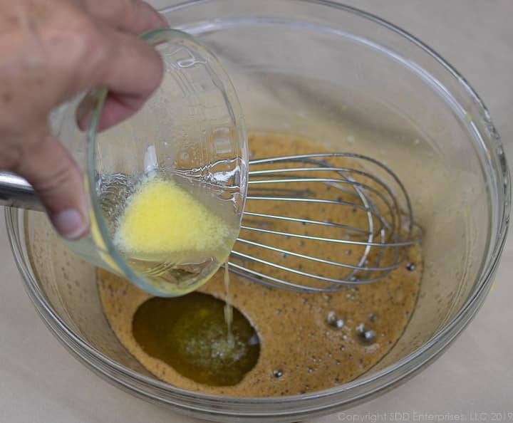 melted butter being poured into eggs and sugar in a clear glass bowl for bread pudding
