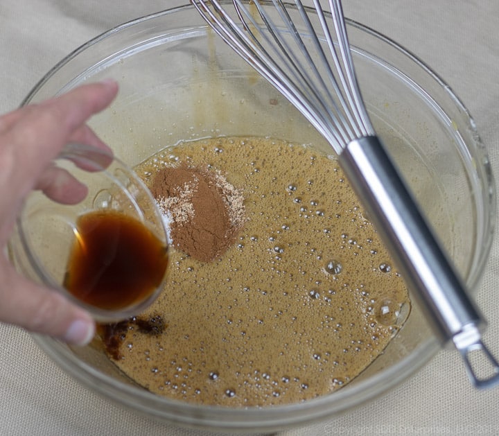 vanilla extract and spices being added to an egg mixture in a clear glass bowl for bread pudding