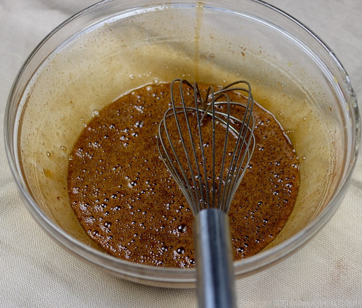 whisked eggs, brown sugar, butter and spices mixed in a clear glass bowl with a whisk for bread pudding