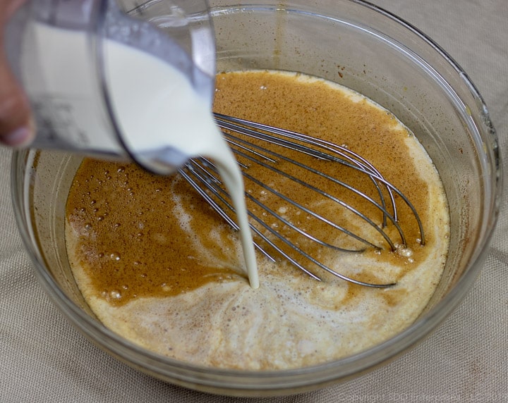 pouring heavy cream into a clear glass bowl filled with egg mixture and milk for bread pudding