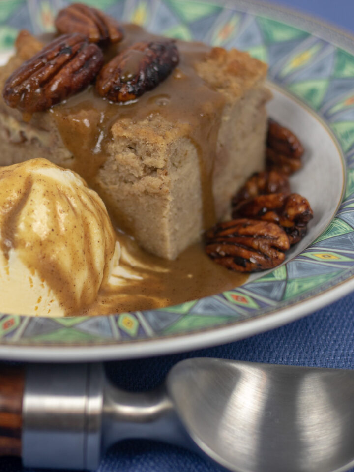 bread pudding with cane syrup rum sauce and glazed pecans with a scoop of vanilla ice cream in a bowl with green trim and an ice cream scooper