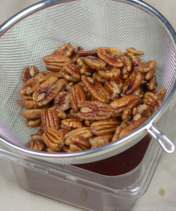 pecans marinated in rum being strained into a container