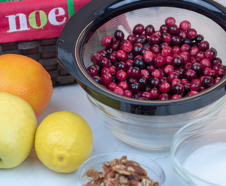 fresh cranberries in a strainer, an orange, apple and lemon and pecan pieces with white background and christmas decoration