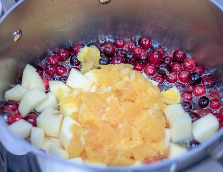 orange pulp and apples added to a sauce pan with cranberries and orange juice for cranberry relsih