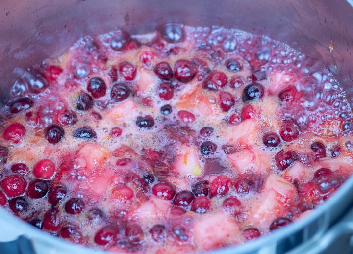 cranberries and fruit simmering in a sauce pan for cranberry relish