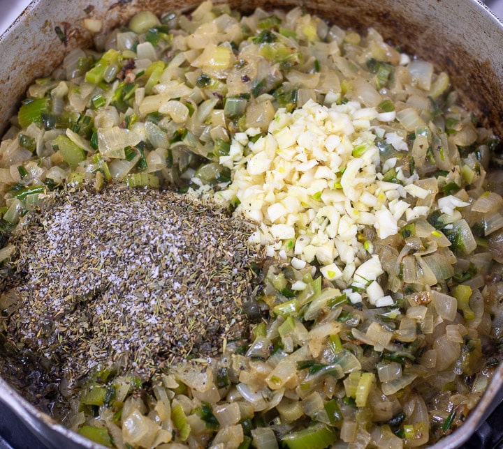herbs and garlic added to frying onions and celery in a frying pan for oyster dressing